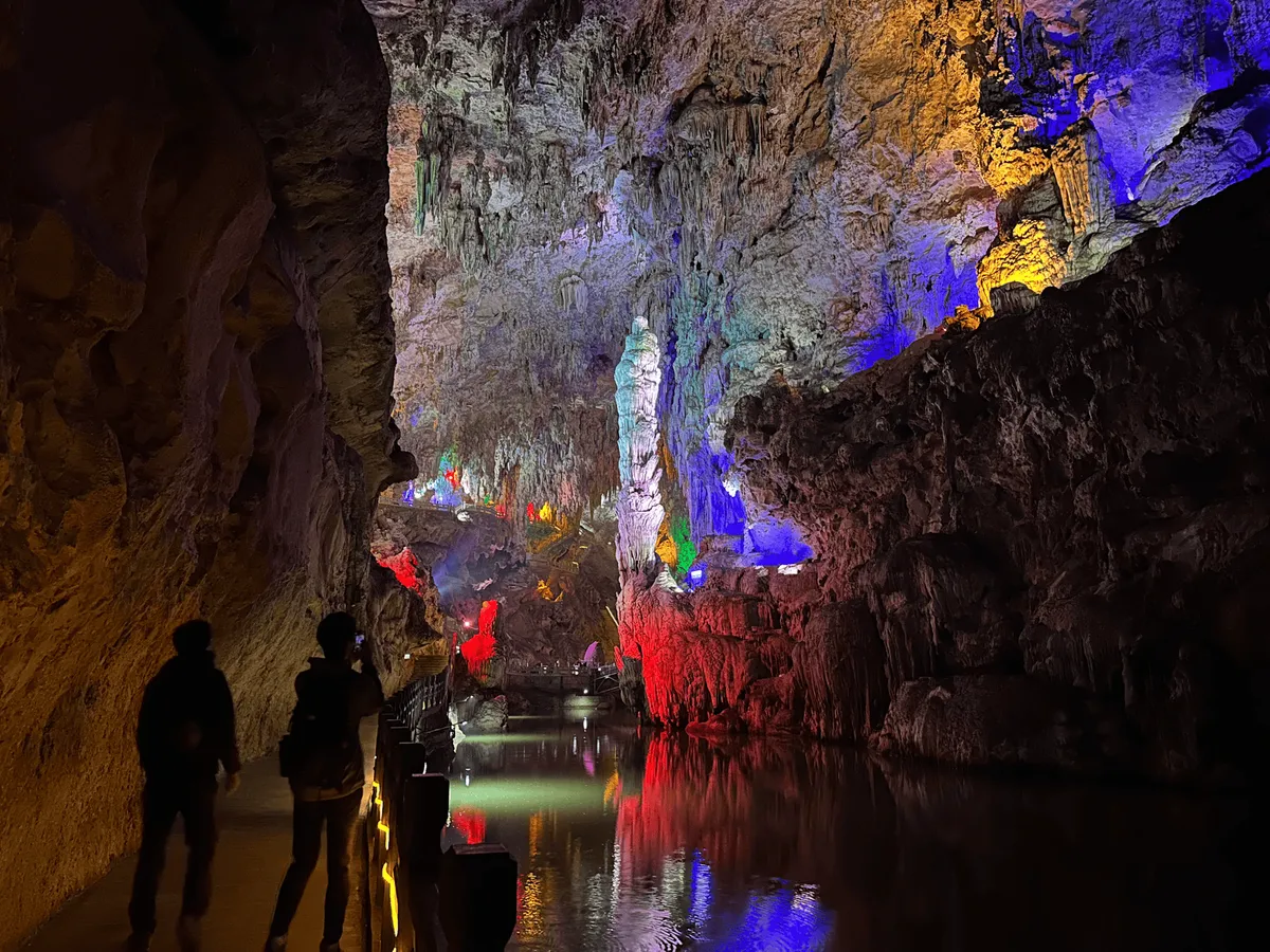 Entrance to the cave, featuring a canal of water in the middle and the walls lit up with multicoloured lights. 