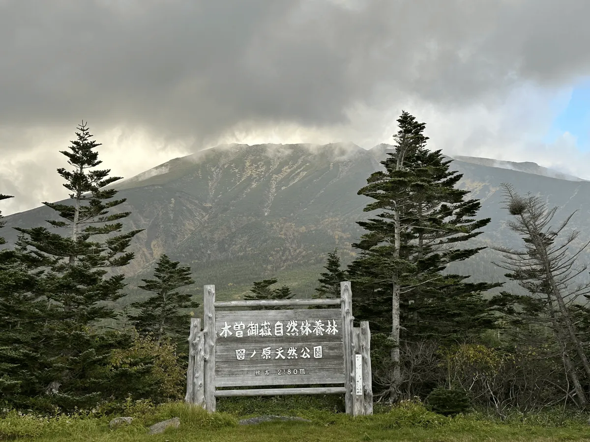 The peak of Mt Ontake, mostly visible. In the front is a wooden sign, marking the area as a nature park.