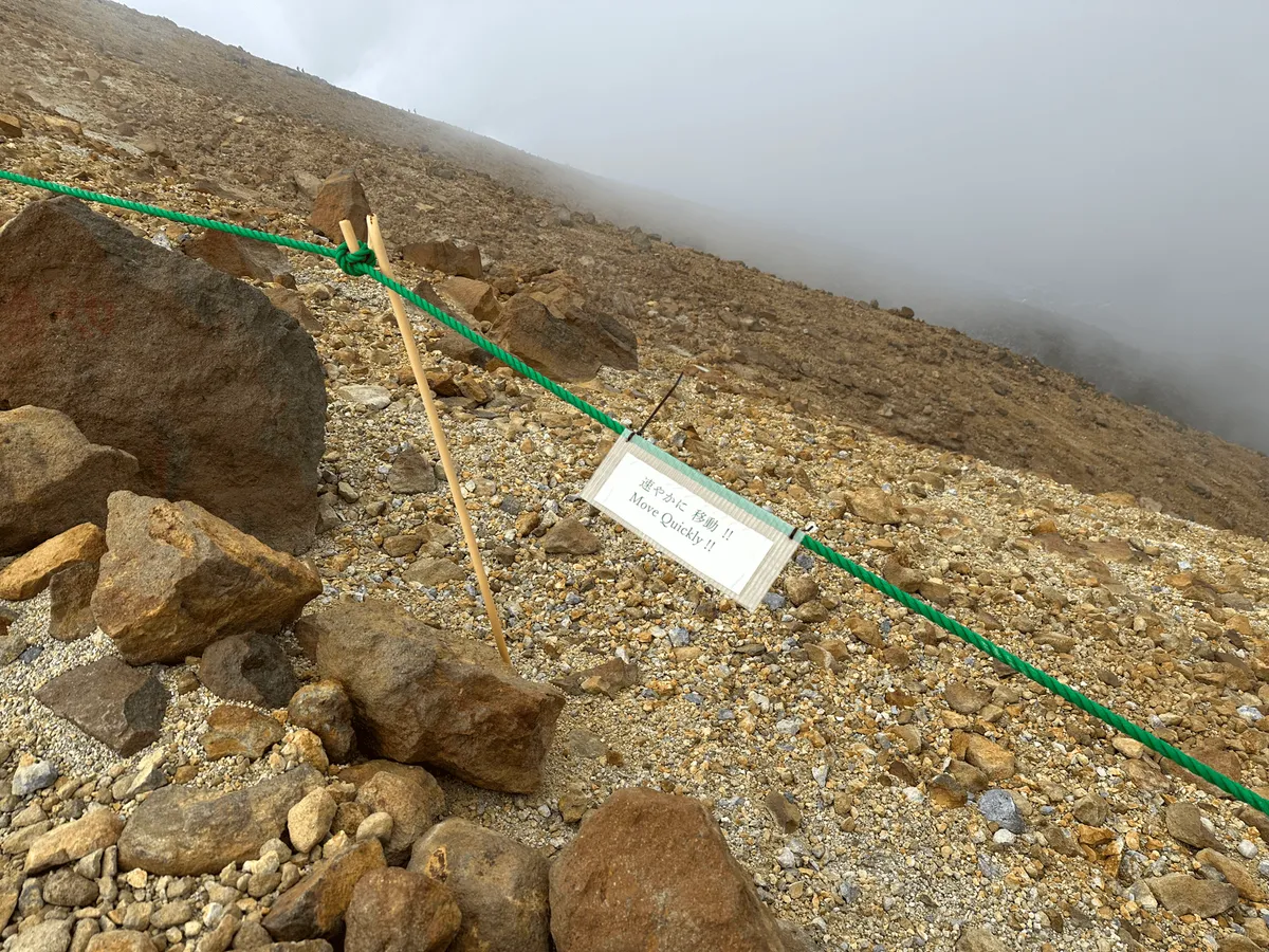 A little white sign saying move quickly, attached to a green rope fencing off the trail.