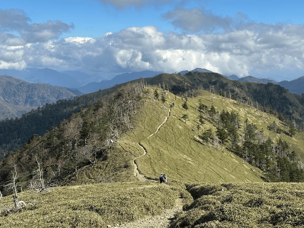 The hiking trail stretches out into the green hills below, and up onto another mountain peak.