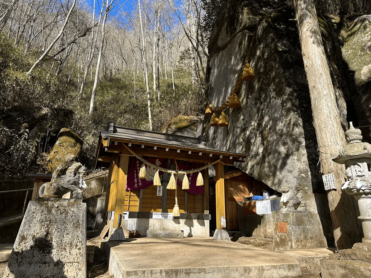 A small shrine building, with a very large rock next to it.