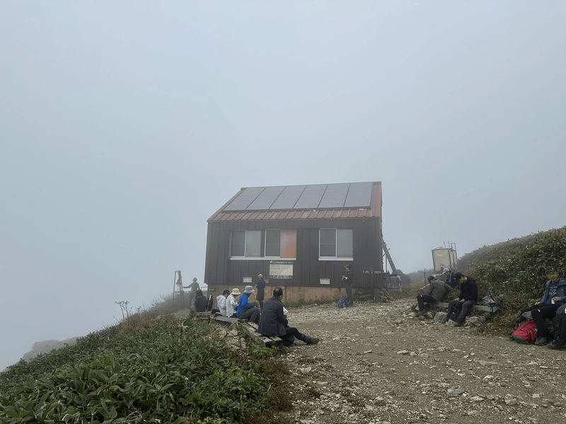 A smal brown building, partially obscured in mist. Quite a few people sitting down around it.