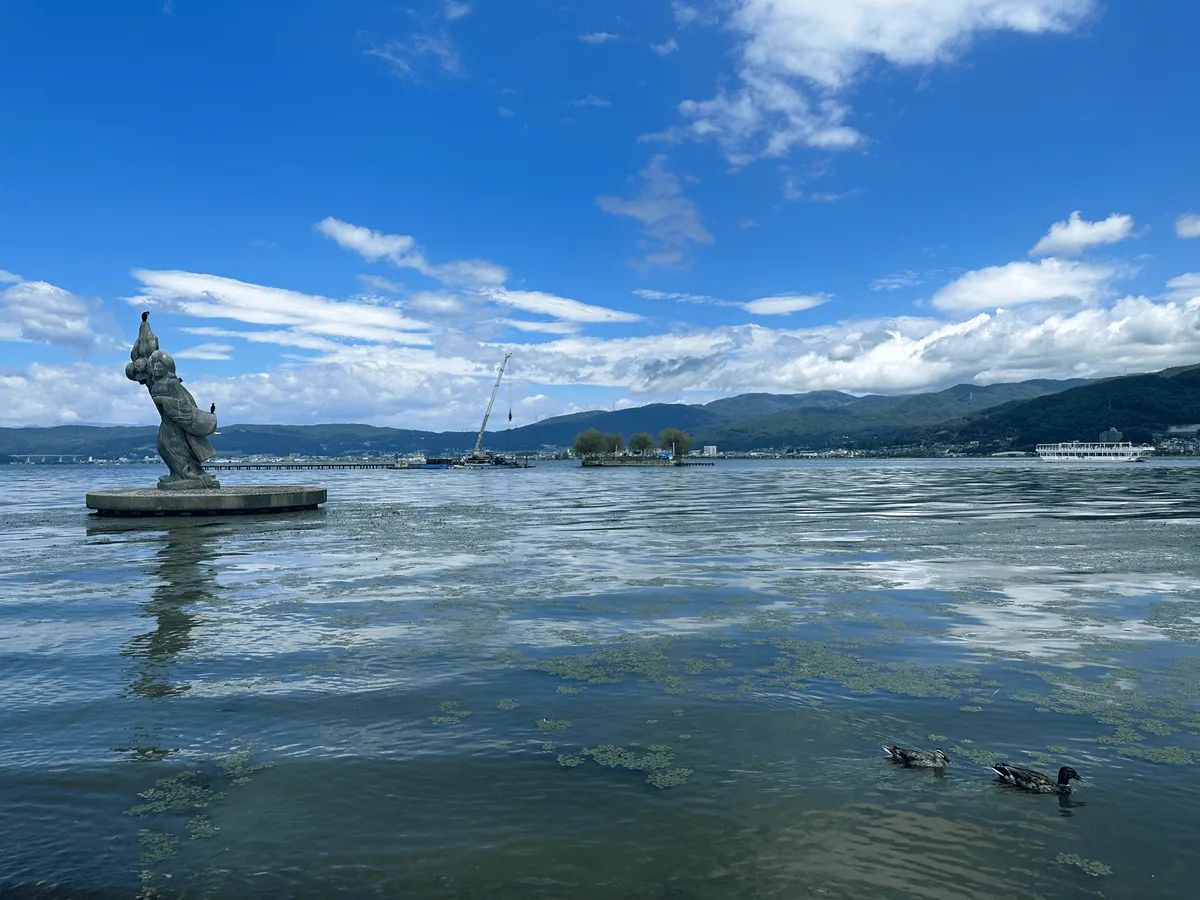 A large lake with some ducks and a statue of a woman