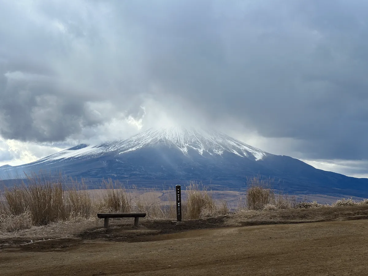 Mt Fuji in the background. In the foreground is a bench and a peak marker.