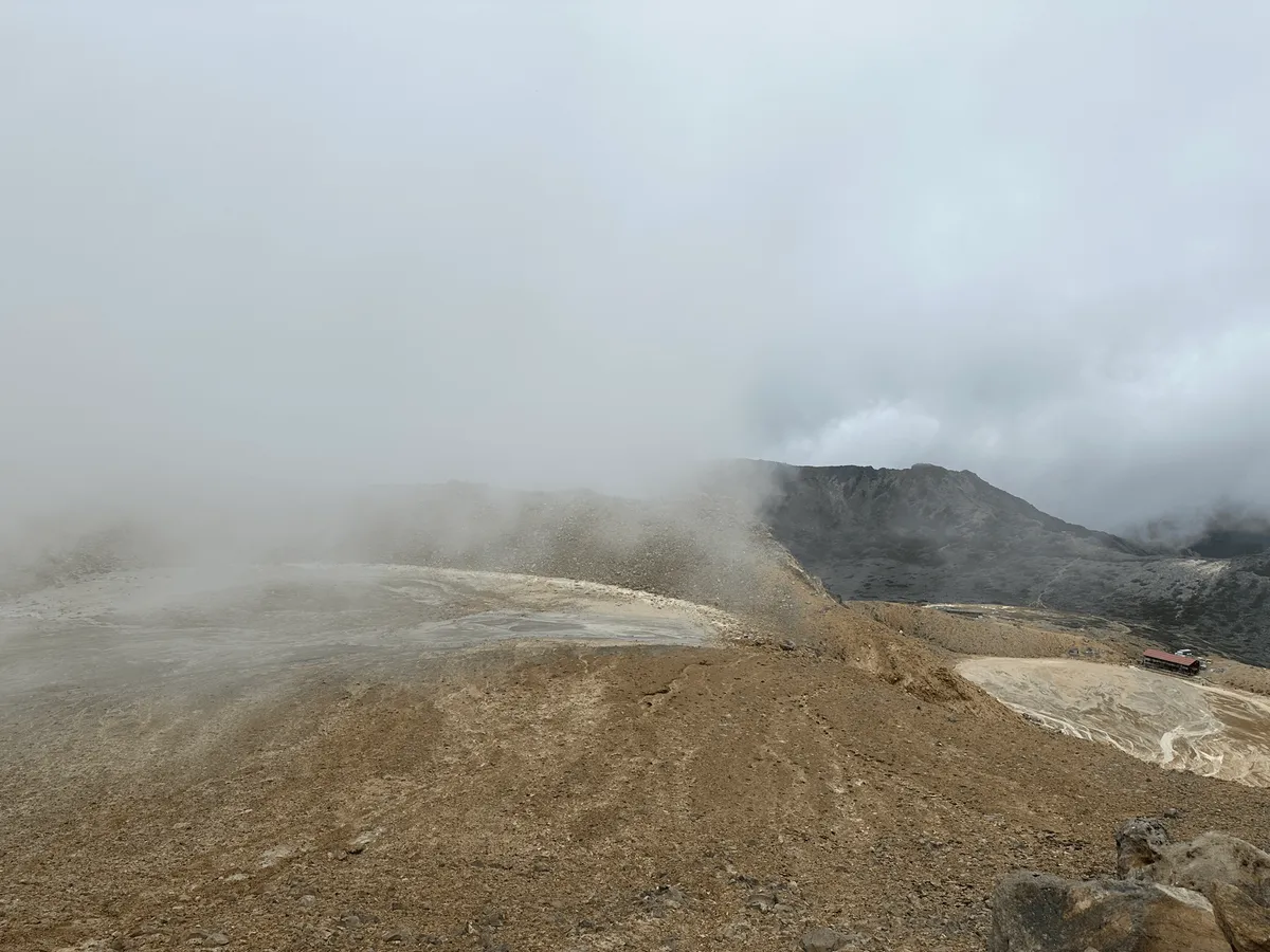 A half-fog-obscured view of a brown plain below with a red-roofed building on the right.