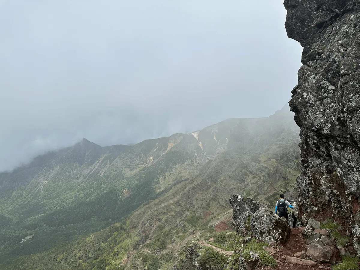 The trail is narrow with a large rock face on the right, with a drop-off on the left.