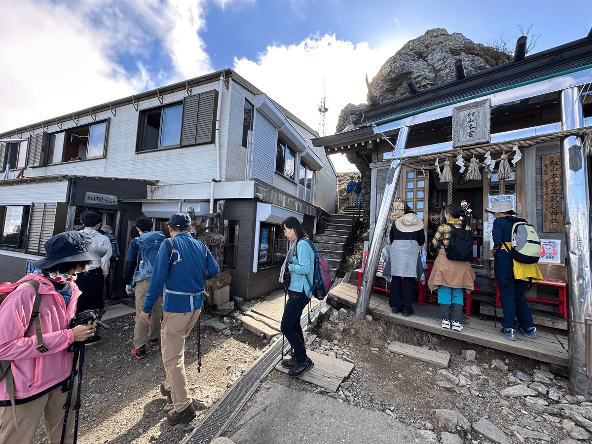 A mountain hut building on the left with a silver torii gate and shrine on the right. 