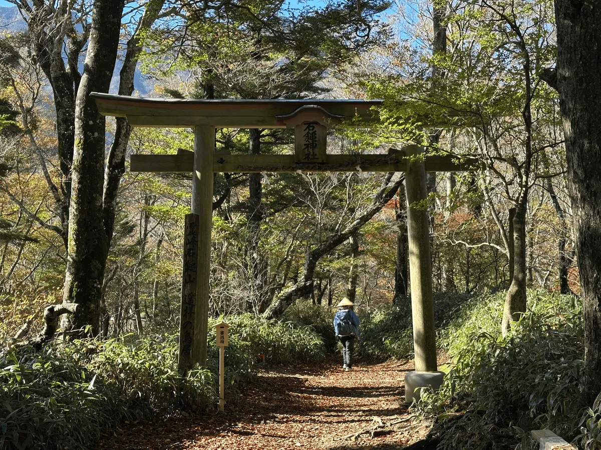 A Torii gate with a hiker wearing a straw hat passing through it