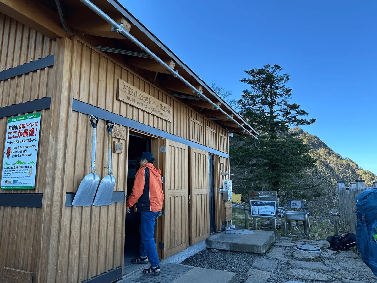 A wooden toilet building, with large shovels attached to the front.