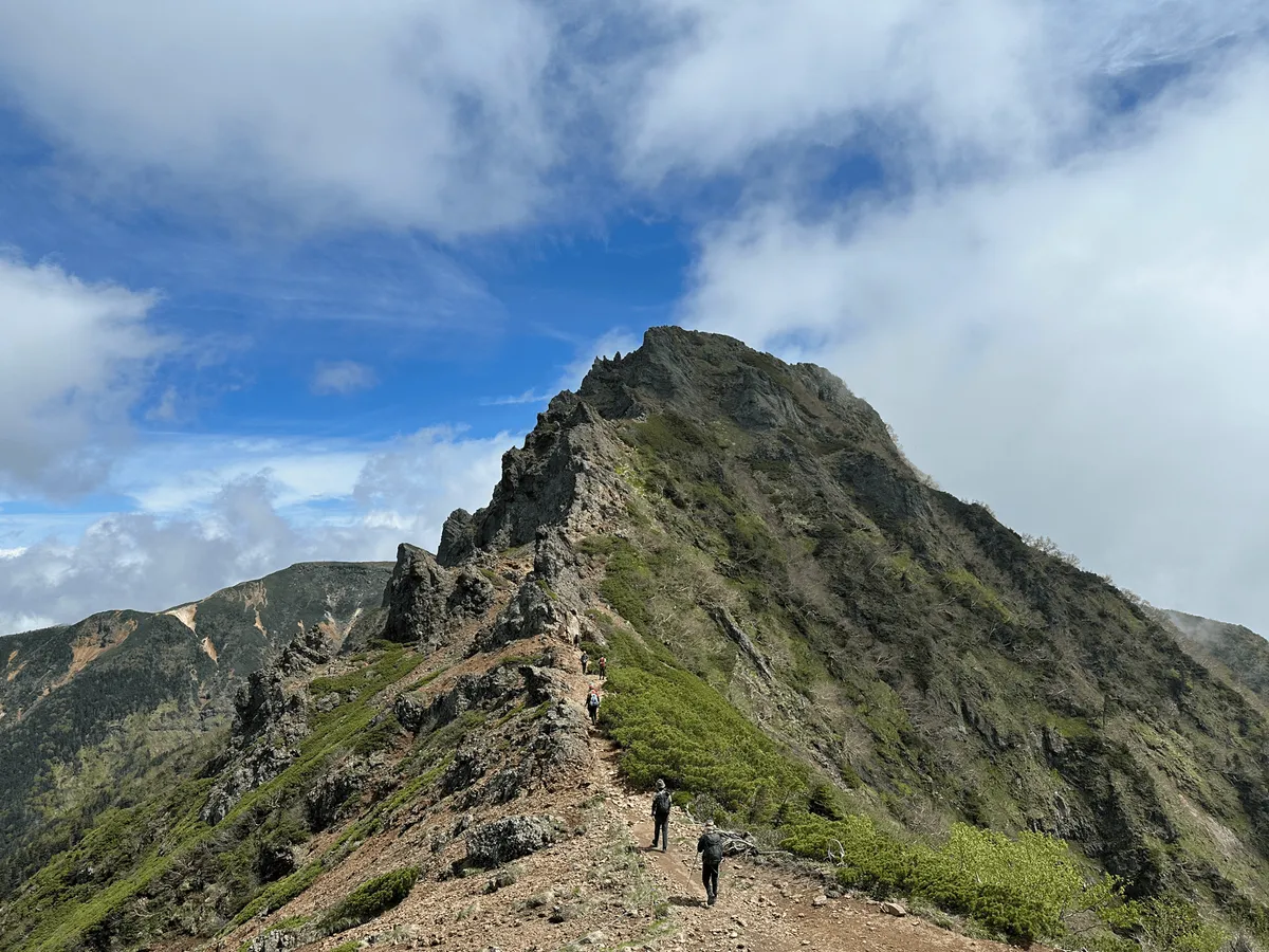 Some people walking along a trail, towards a little peak